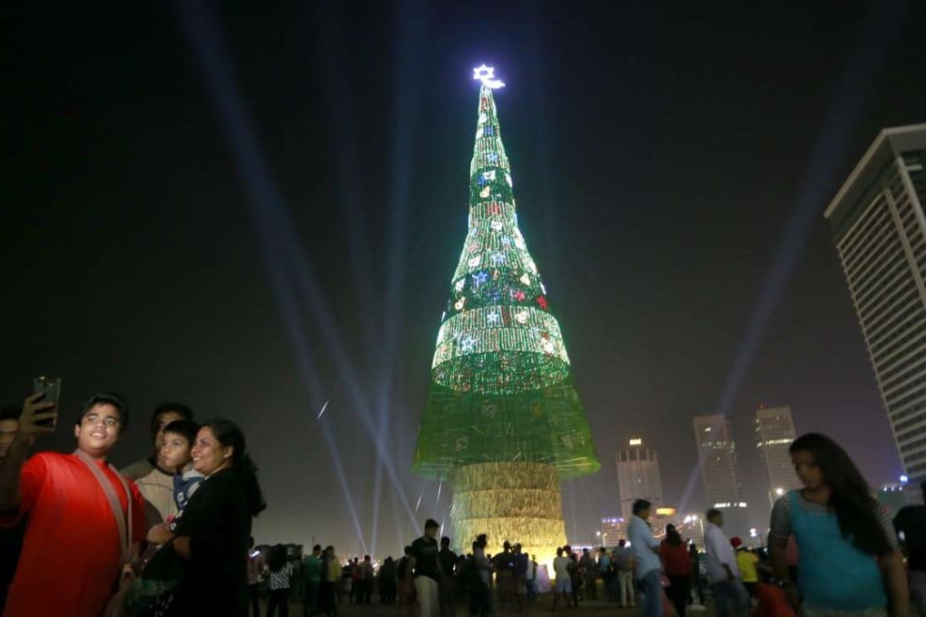 A Sri Lankan family takes photographs standing near an enormous artificial Christmas tree as others gather around it in Colombo, Sri Lanka, Saturday, Dec. 24, 2016. Sri Lanka has unveiled a towering Christmas tree, claiming to have surpassed the world record for the tallest artificial Christmas tree. (AP Photo/Eranga Jayawardena)