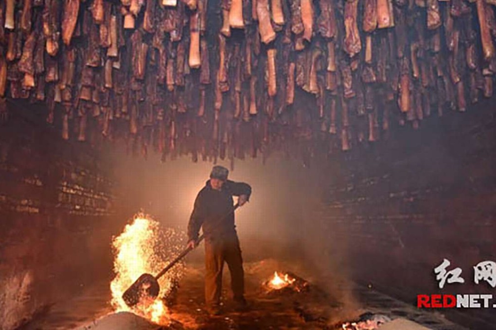 A man stokes a fire, above which pork is hung to smoke during the process of making Hunan-style bacon. Photo: Rednet.cn