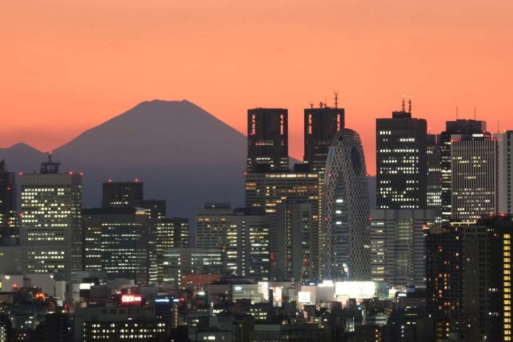 Mount Fuji, Japan's highest mountain, towers behind skyscrapers in Tokyo's Shinjuku area during sunset.
