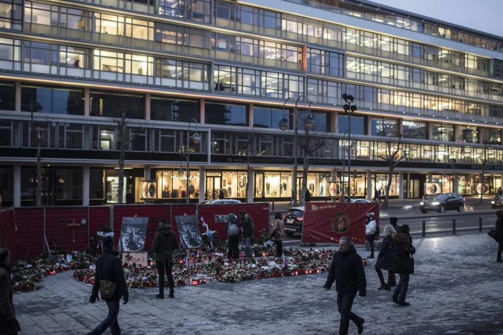 People walk past flowers and candles mourners placed on the Breitscheid square in Berlin,. Photo: EPA