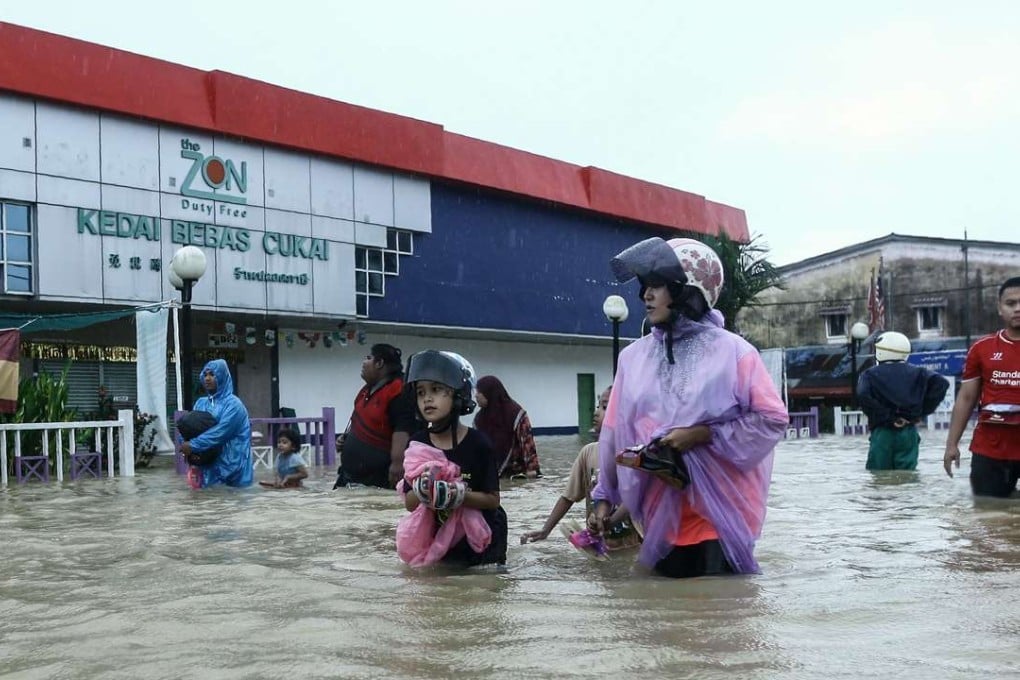 People wade through floodwaters past a duty free shop in Malaysia's northeastern town of Rantau Panjang, which borders Thailand, on January 3, 2017. Emergency services in Malaysia deployed boats and trucks on January 3, as thousands of villagers were stranded after four days of heavy rain caused flooding in east coast states, officials said. / AFP PHOTO / STR / Malaysia OUT