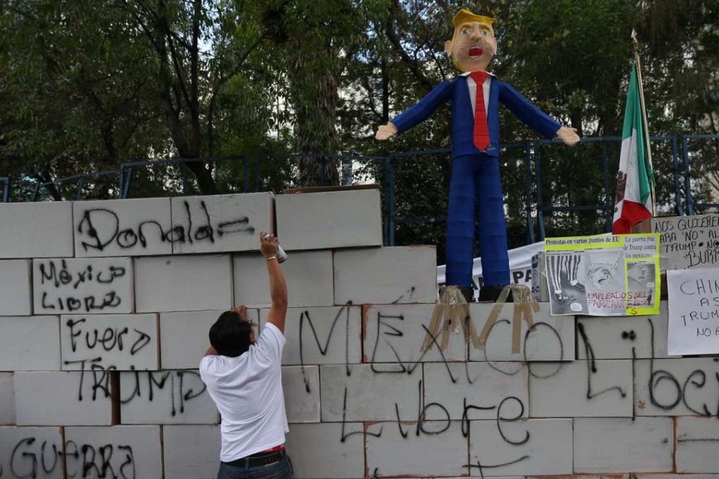 A demonstrator writes on symbolic wall as is seen a pinata representing the US President Donald Trump during a protest in Mexico City. Photo: Reuters