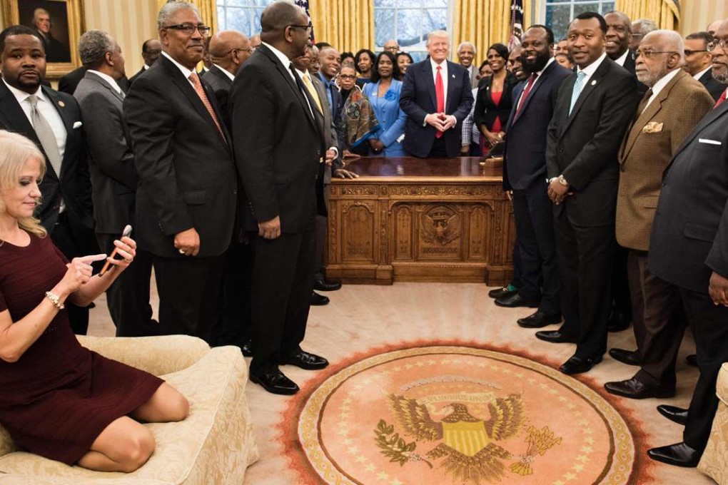 Counsellor to the US president Kellyanne Conway checks her phone after taking a photo as US President Donald Trump and leaders of historically black universities and colleges pose for a group photo in the Oval Office. Photo: AFP