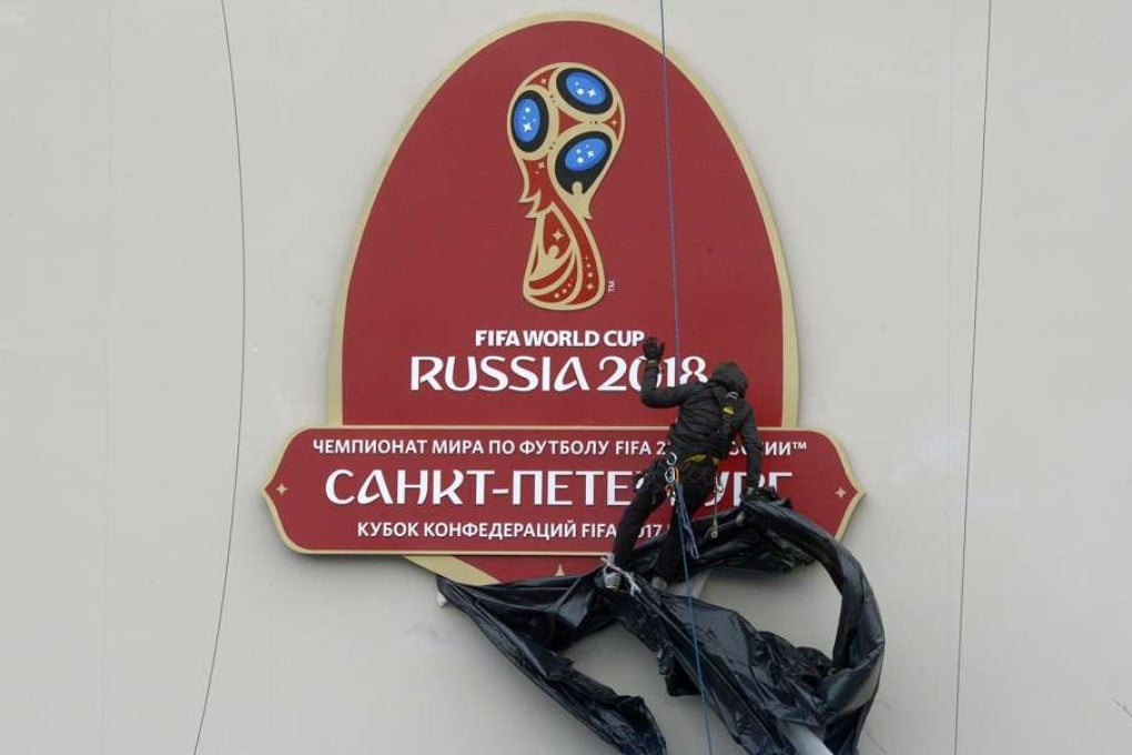 An alpinist removes a wrap from the FIFA World Cup 2018 logo before a ceremony marking the last 100 days until the start of the FIFA Confederations Cup 2017 at the new football stadium at Krestovsky island, also known as the Zenit Arena in Saint Petersburg on March 9, 2017. / AFP PHOTO / OLGA MALTSEVA