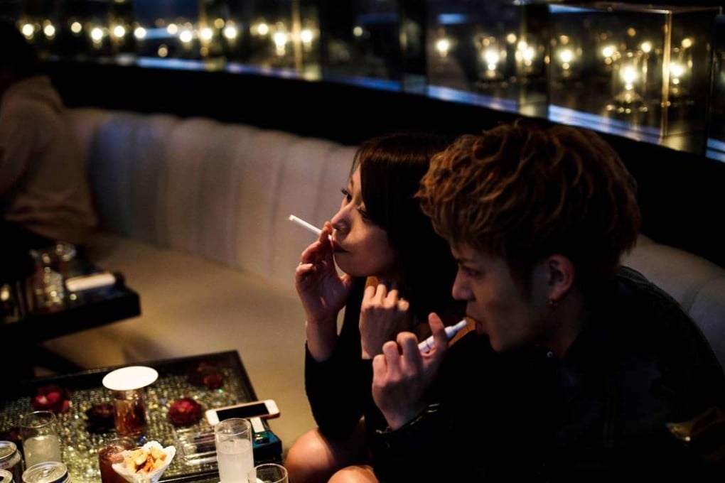 A woman smokes a cigarette, while her friend uses an electronic cigarette, inside a club in the Kabukicho district of Tokyo. Photo: AFP