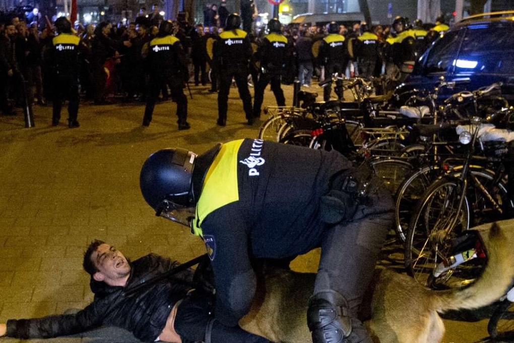 A Dutch riot policeman tries to get his dog to let go of a man after riots broke out during a pro Erdogan demonstration at the Turkish consulate in Rotterdam. Photo: AP