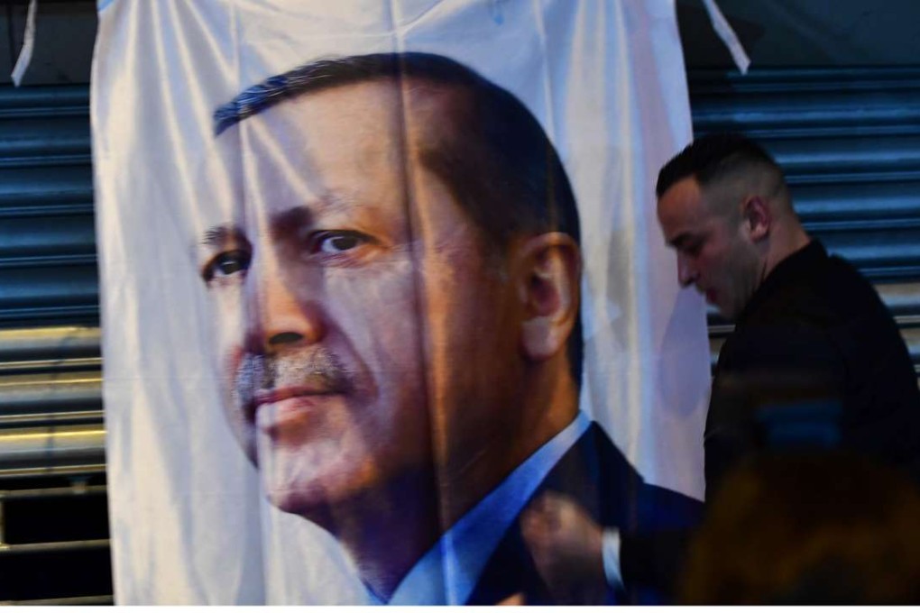 A man gestures in front of a flag bearing a portrait of Turkish President Recep Tayyip Erdogan. Photo: AFP
