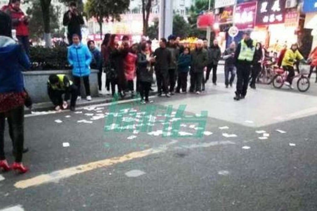 Police in Chongqing pick up yuan notes tossed onto the street by a woman 'in a bad mood' as pedestrians look on. Photo: Handout