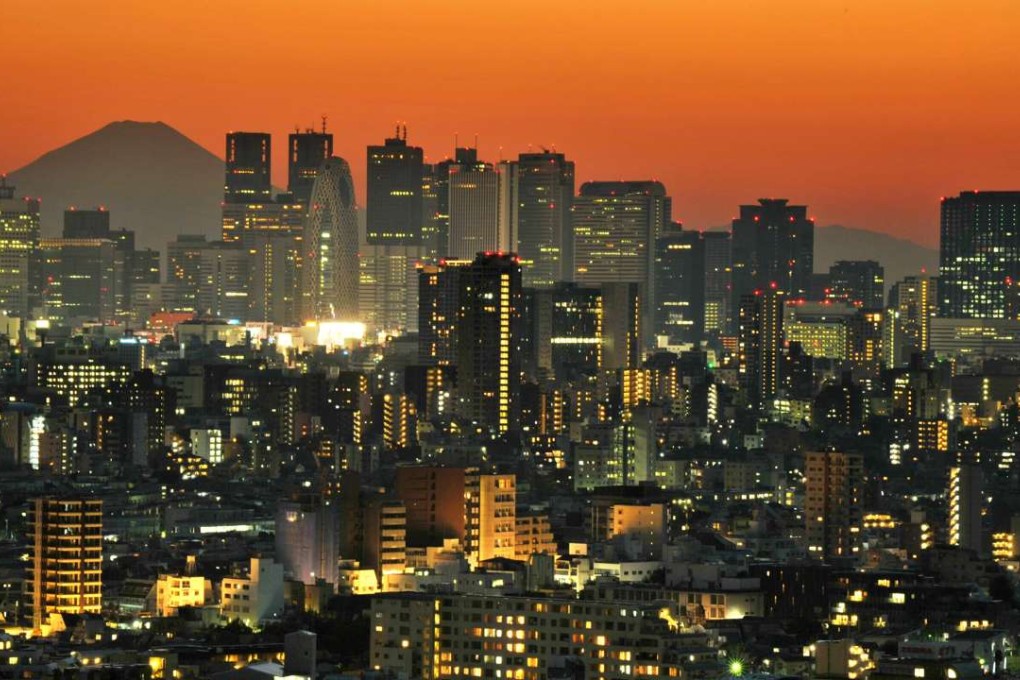 Japan's highest mountain Mount Fuji rises behind brightly lit skyscrapers dotting the skyline of the Shinjuku area of Tokyo at sunset. Photo: AFP