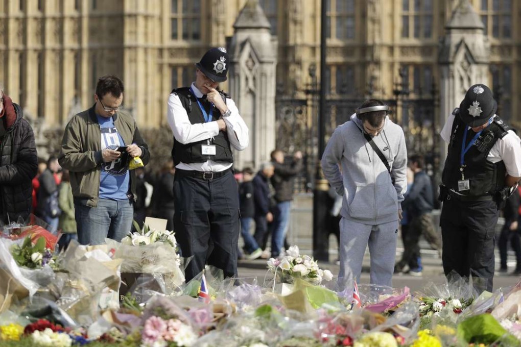 Police officers and members of the public look at the floral tributes to the victims of the Westminster attack placed outside the Palace of Westminster, London, on Monday. Photo: AP