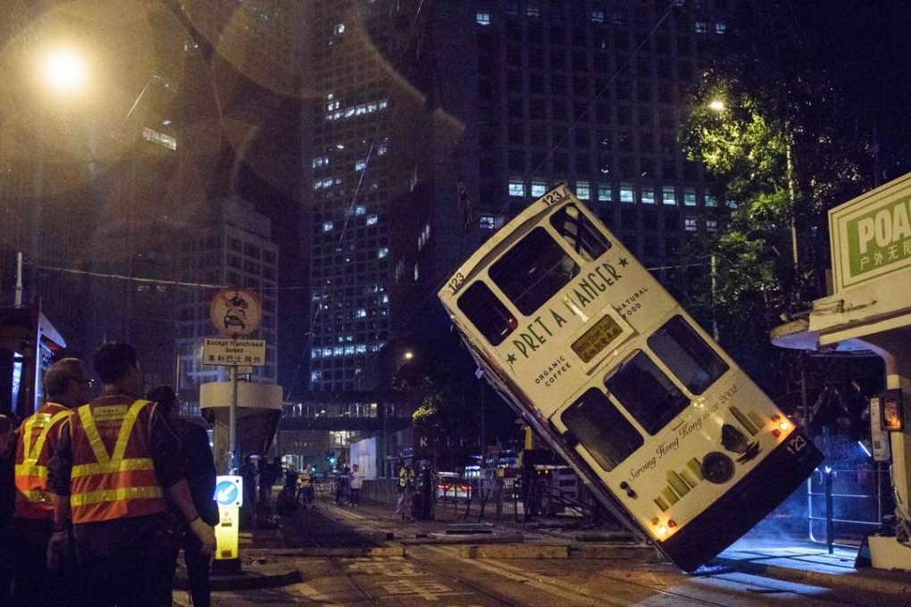 Emergency service personnel watch as a double-decker tram is lifted back up by crane after it tipped over on a main road in Hong Kong on Thursday. Photo: AFP