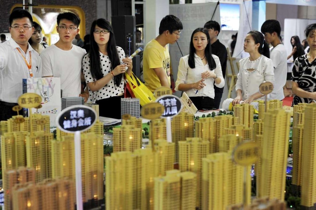 Sales representatives talk to potential buyers in front of a model of a residential complex at a real estate exhibition in Wuhan, Hubei province. Photo: Reuters