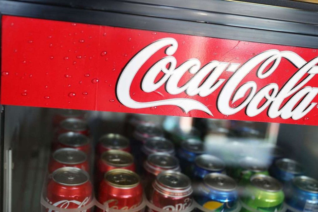 A Coca Cola sign is seen as Coke products are on display in a store as the company announces plans to cut 1200 corporate staff jobs. The announced changes come as the company battles a slide in soda sales which along with higher costs has lead to a 20 per cent drop in quarterly profit. Photo: AFP
