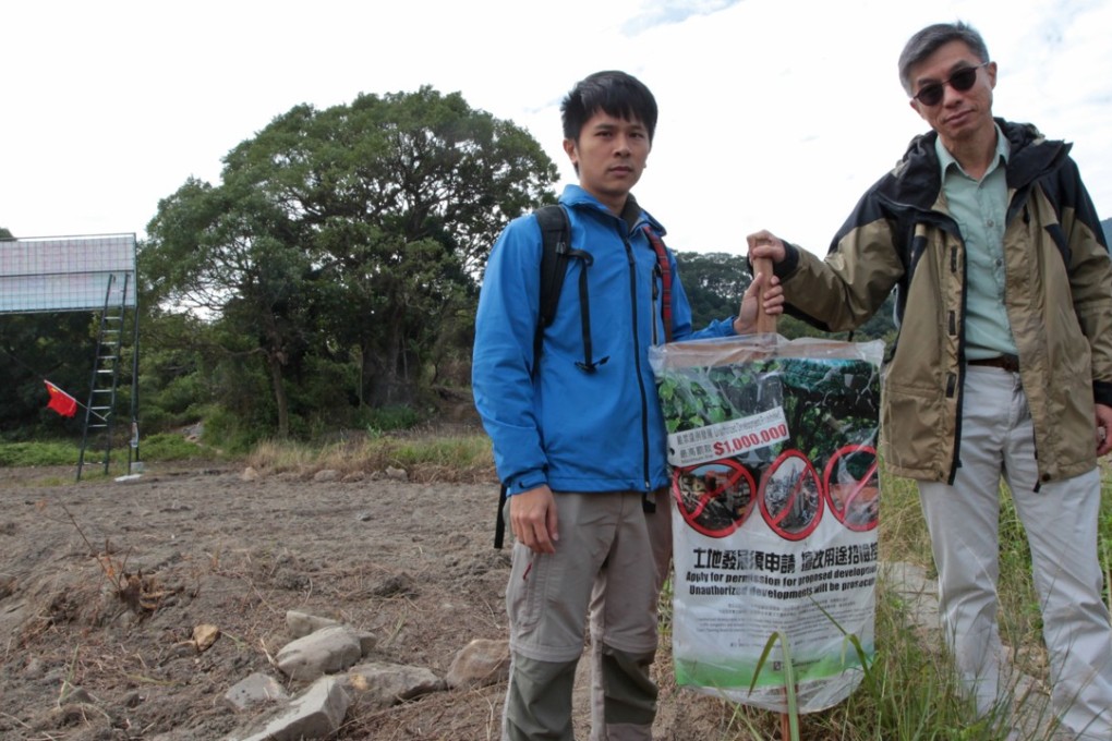 Conservationists Roy Ng Hei-man and Michael Lau Wai-neng beside a government banner on enclaves destruction in Sha Lo Tung, Tai Po. Photo: Bruce Yan