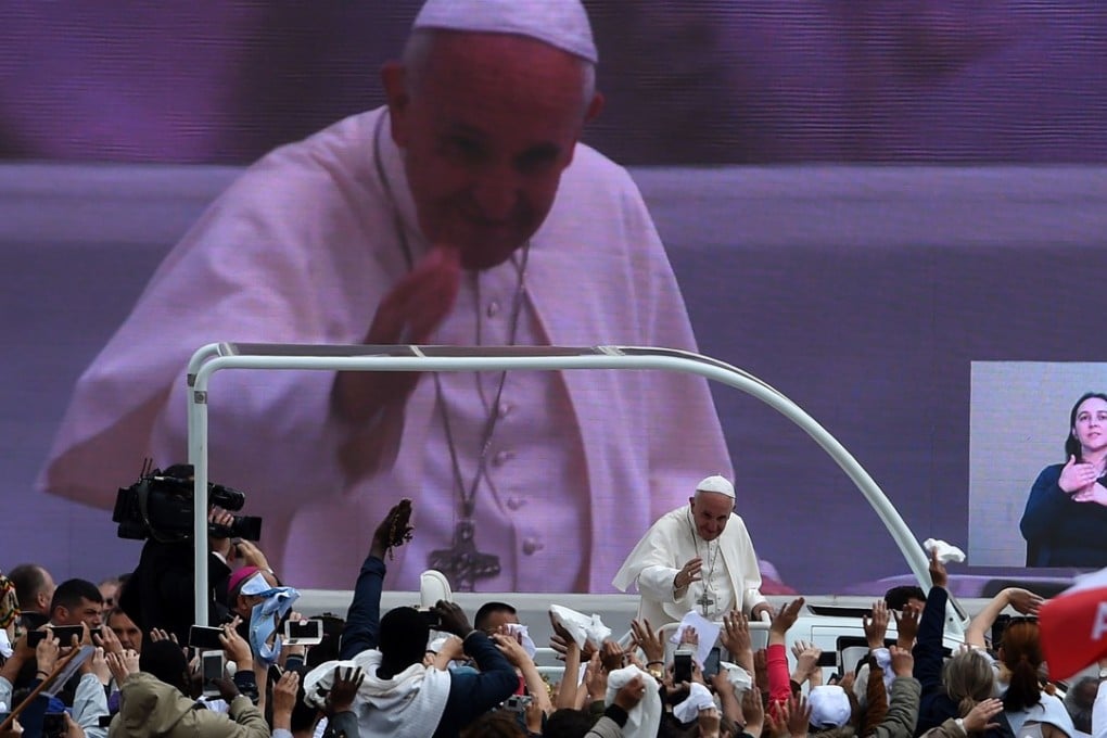 Pope Francis waves to faithful from the popemobile as it passes a massive TV screen covering the event. Photo: AFP