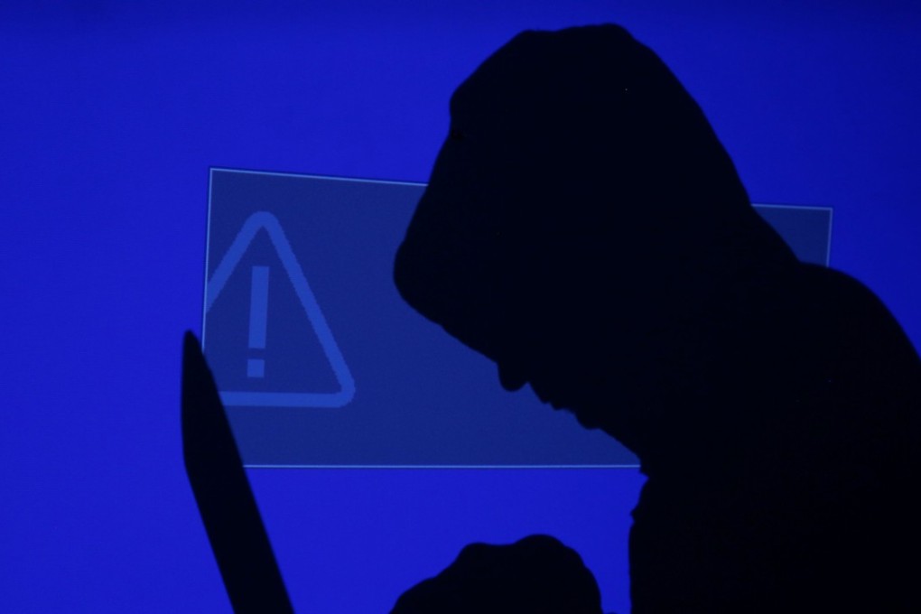 A hooded man holds a laptop computer as a blue screen with an exclamation mark is projected on him in this illustration picture taken on May 13, 2017. Capitalising on spying tools believed to have been developed by the US National Security Agency, hackers staged a cyber assault with a self-spreading malware that has infected tens of thousands of computers in nearly 100 countries. Photo: Reuters