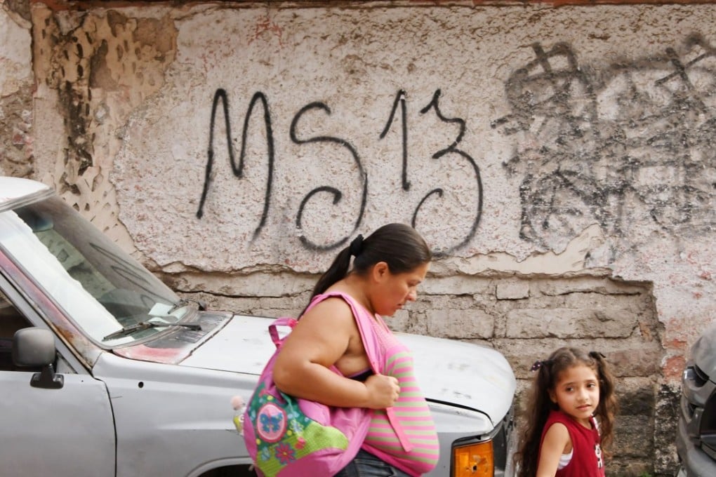 Local residents pass by grafitti made by the Mara Salvatrucha gang in the MS-13-controlled El Bosque neighborhood in Tegucigalpa. Hundreds of people are fleeing due to gang violence in Honduras. Photo: AFP