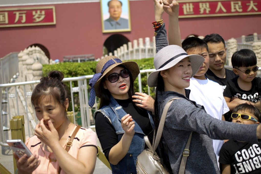 Women gesture as they pose for a photo in front of Tiananmen Gate during the May Day holiday in Beijing. A survey showed that Chinese are choosing work rather than have children. Photo: AP