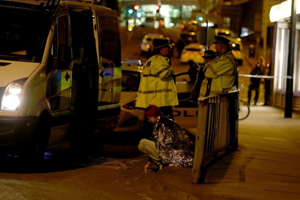 A woman sits in the street in a blanket near the Manchester Arena as police guard the area following an explosion on Monday night. Photo: EPA