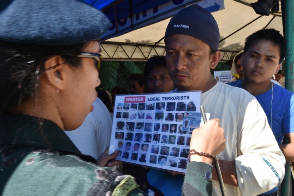 A police officer checks the identity of a resident against a chart with images of ‘local terrorists’ at a checkpoint at the entrance to Iligan city. Photo: AFP