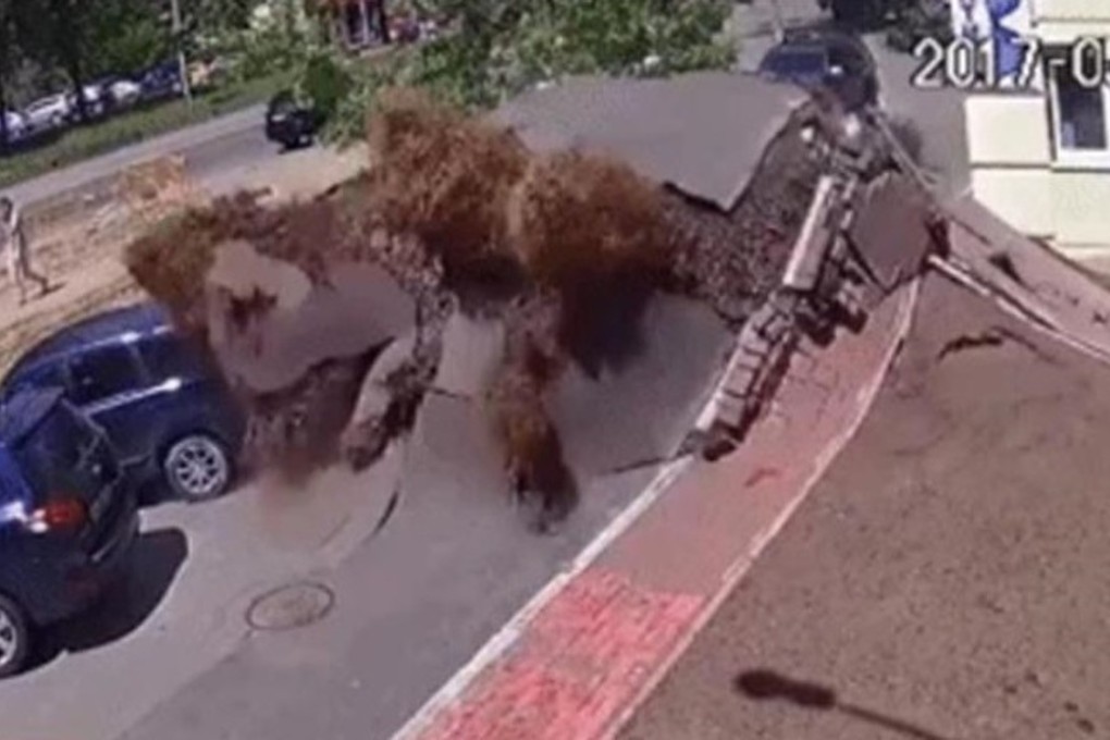 A woman walks past the bizarre scene of a carpark expanding like a balloon in Kiev, Ukraine, moments before a massive and muddy explosion on Monday. Photo: YouTube / Live Leak