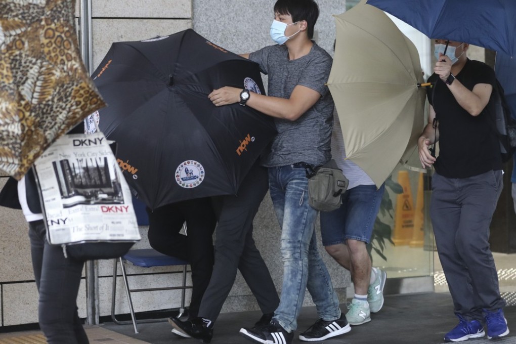 Defendant Ng Ting-kai (in dark shoes under black umbrella) was escorted by an unidentified man in a mask as they left the West Kowloon Court. Photo: Edward Wong