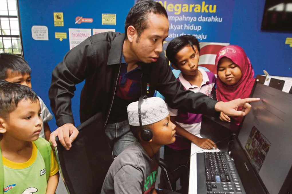 Pusat Internet 1Malaysia manager Mohd Shamsul Mohd Samsuddin (centre) teaching children to use a computer, in Kampung Kempadang, Kuantan. Photo: Farizul Hafiz Awang