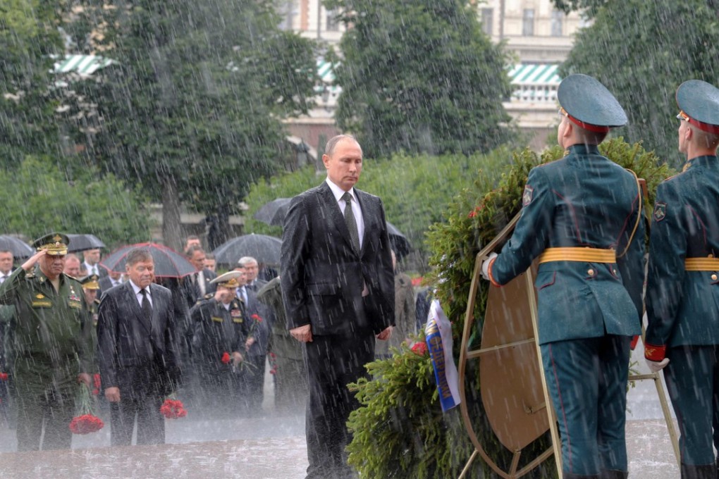 Russian President Vladimir Putin (C) stands under a pouring rain during a wreath-laying ceremony marking the 76th anniversary of the Nazi German invasion, by the Kremlin walls in Moscow. The EU extended punishing economic sanctions against Moscow due to the situation in the Ukraine. Photo: AFP
