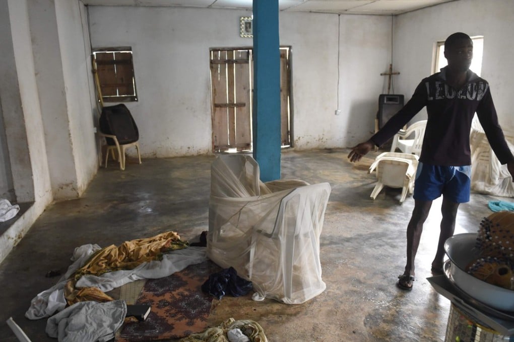 A man points to blood-stained clothes, drums, bibles and hymn books on the bare floor, where shadowy gang dubbed the Badoo killed four worshippers in the Crystal Church of God at Owode Onirin in Lagos. Photo: AFP