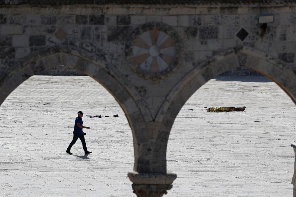 An Israeli policeman walks past a body after an attack at the Al-Aqsa mosque compound. Photo: AFP
