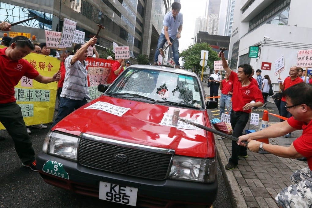 Taxi drivers smash a taxi to call on the government to ban car-rental services, outside Wan Chai Tower on July 24, 2015. For all the government’s free-market claims, it is often held hostage by vested interests. Photo: Dickson Lee