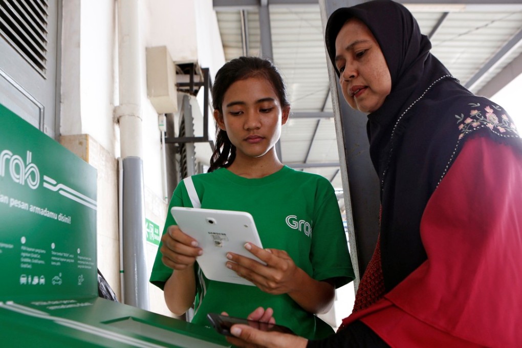 An employee of the online ride-hailing service Grab helps a customer order transport at a kiosk at Manggarai train station in Jakarta, Indonesia. Photo: Reuters