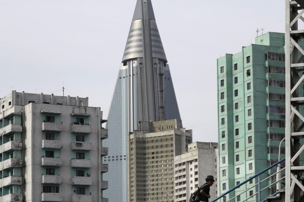 A man climbs the stairs of an overpass at a road intersection while residential buildings and the unfinished Ryugyong Hotel is seen in the background. Photo: AP
