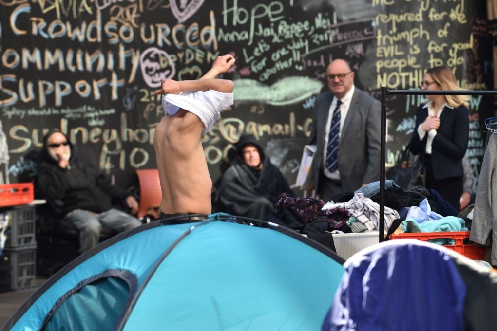 A homeless man gets dressed after stepping out of his tent set up in Martin Place as office workers walk past. Photo: AFP