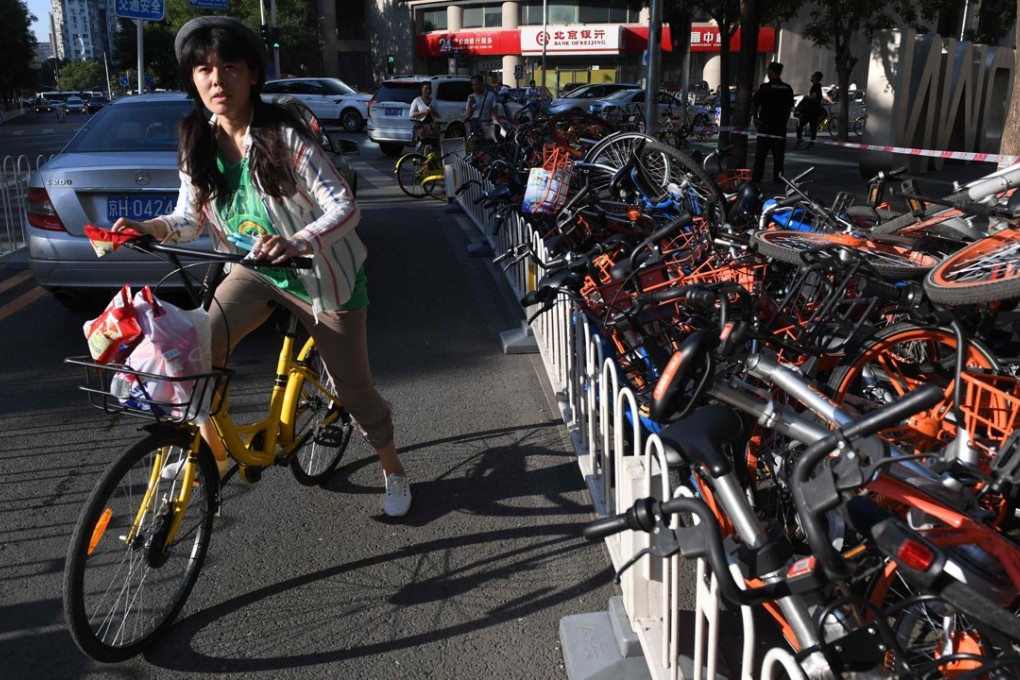A woman rides past a bicycle lane blocked with discarded shared bikes in Beijing. Photo: AFP