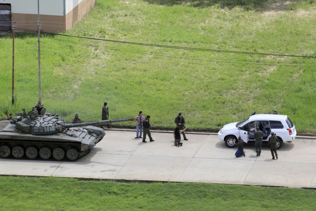 Soldiers detain the passengers of a vehicle, whose passengers kneel at gunpoint, on the Paramacay military base in Valencia, Venezuela, on Sunday. Photo: AP