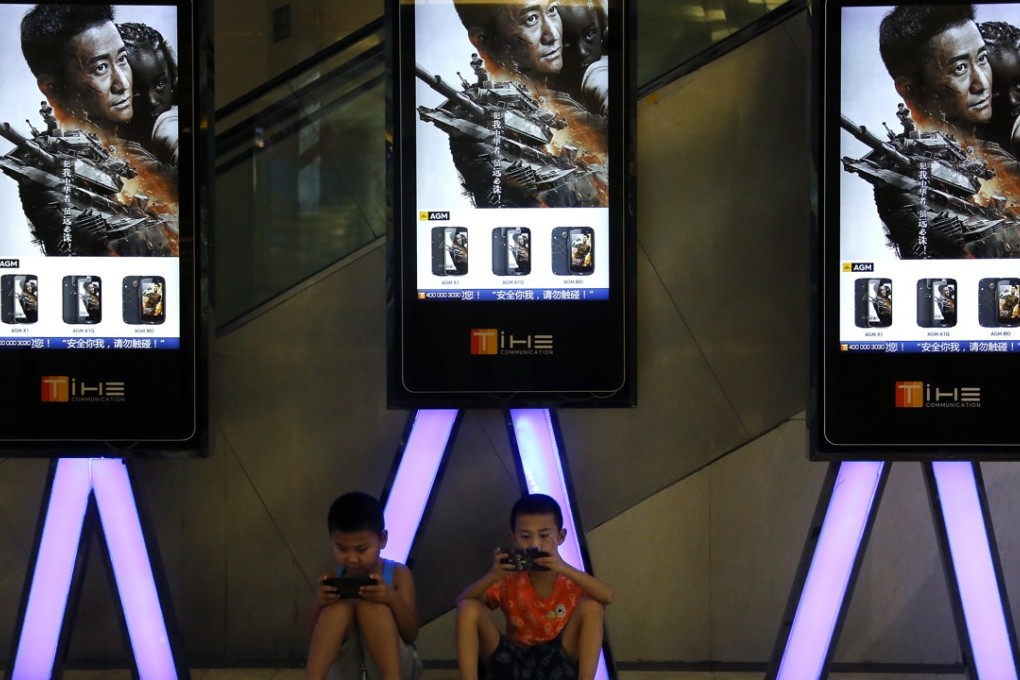 Children use smartphones near monitors displaying the Chinese action movie Wolf Warrior 2 at a cinema in Beijing. The movie had grossed more than 5 billion yuan at the box office by Sunday. Photo: AP