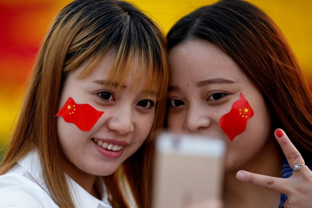 Girls wearing Chinese flags on their cheeks take pictures as people gather in Tiananmen Square to celebrate National Day marking the 67th anniversary of the founding of the People's Republic of China, in Beijing October 1, 2016. Photo: Reuters