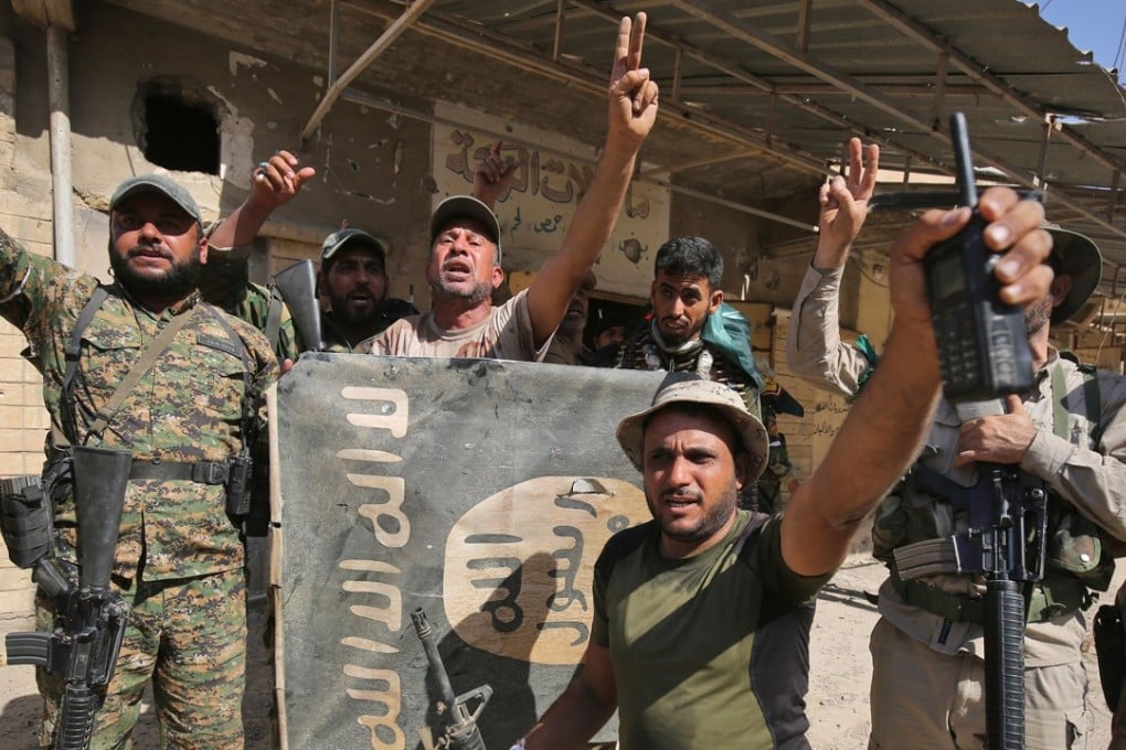 Fighters of Hashed Al-Shaabi (Popular Mobilisation units) flash the victory gesture as they hold upside down a banner bearing the logo of Islamic State (IS) group, during the advance in the town of Tal Afar, west of Mosul. Photo: AFP