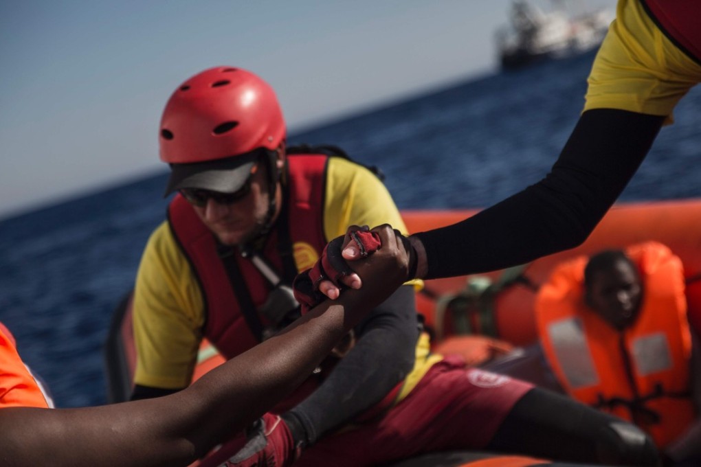 A member of Spanish NGO Proactiva Open Arms (right) helps an African migrant board a rescue boatin the Mediterranean Sea off Libya on August 1. Photo: AFP