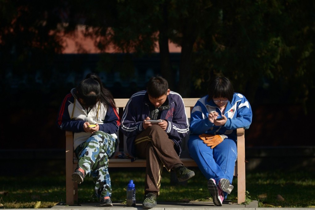 A group of Chinese young people play on their mobile phone as they rest on a bench at a park in Beijing on November 7, 2013. Photo: AFP