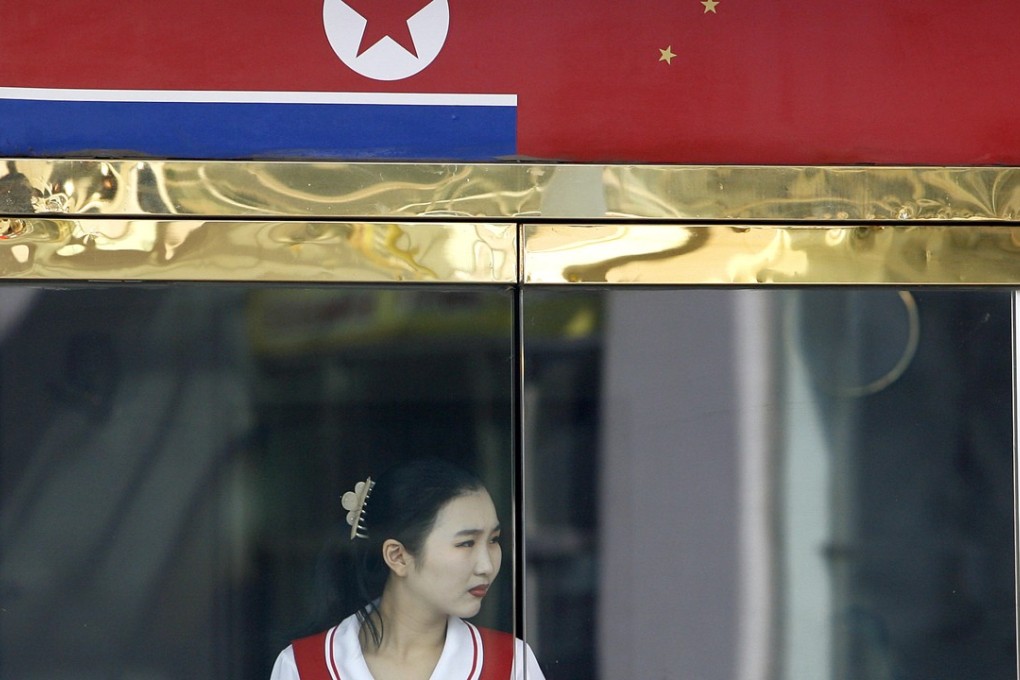 A North Korean waitress stands under the flags of China and North Korea at a Korean restaurant in the Chinese border city of Dandong. Photo: AFP/LIU JIN