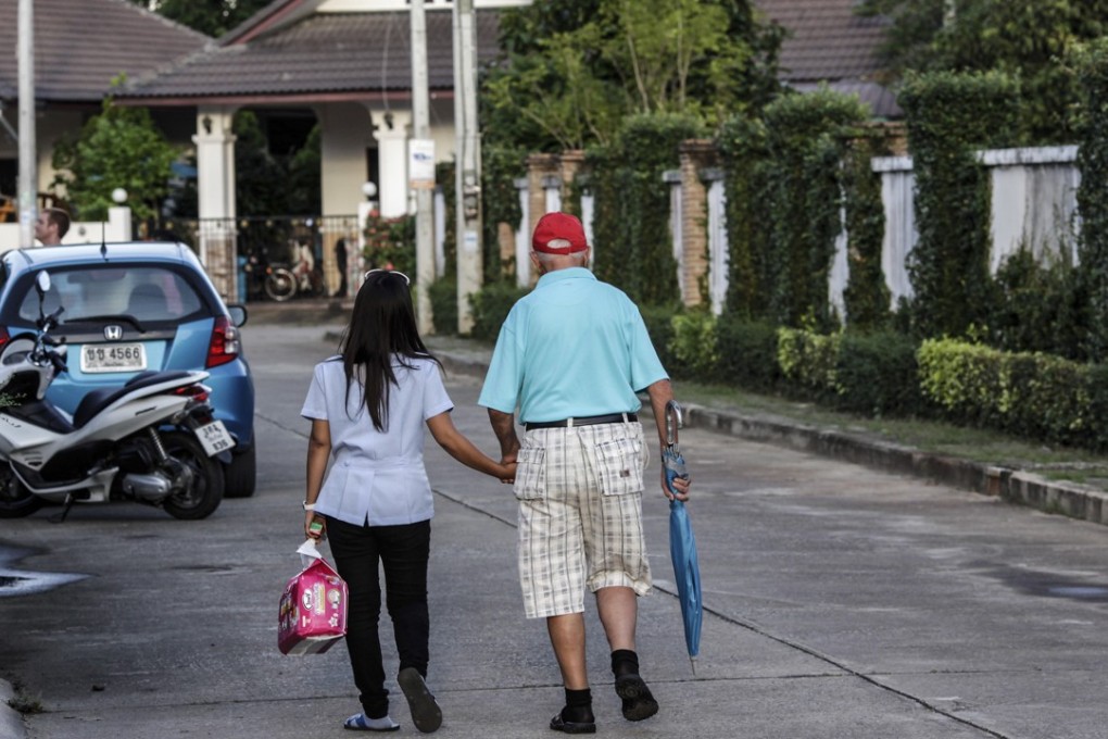 A nurse holds the hand of her patient as they walk through Faham village on the outskirts of Chiang Mai. Photo: Dario Pignatelli