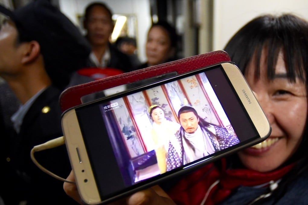 A passenger watches a programme on her mobile phone during a train journey. Xinhua