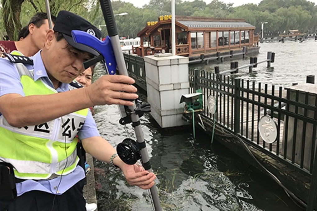 Police officer Zhou Xiangjun has adapted a fishing rod to help him retrieve mobile phones dropped in West Lake, a popular tourist attraction in eastern China. Photo: Handout