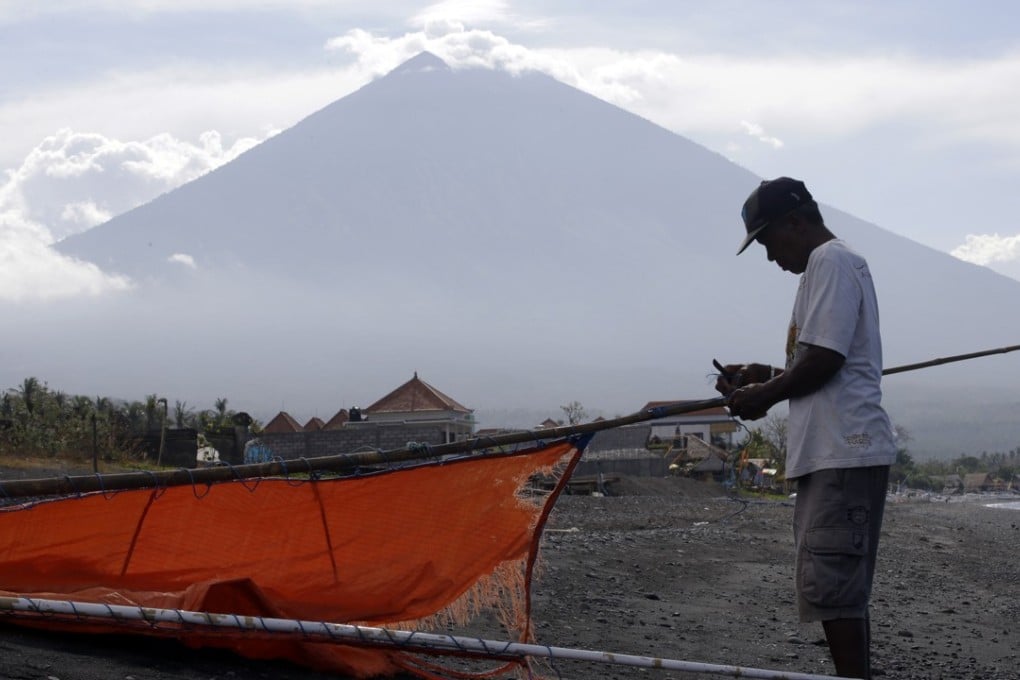 A fisherman repairs his sail with Mount Agung volcano in the background in Karangasem, Bali, Indonesia. Chinese tourism numbers are up for the year on the Indonesian island, but the threat of a volcanic eruption is causing many cancellations. Photo: AP