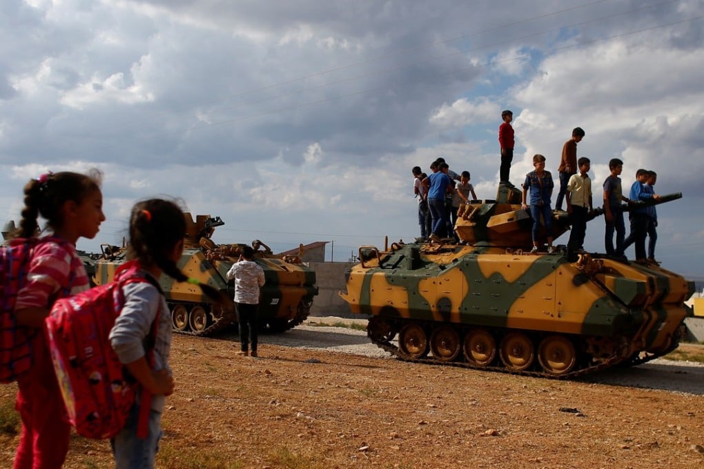 Children watch as a group of boys stand on top of a Turkish military vehicle as a convoy passes through their village on the Turkish-Syrian border line in Reyhanli. Photo: Reuters