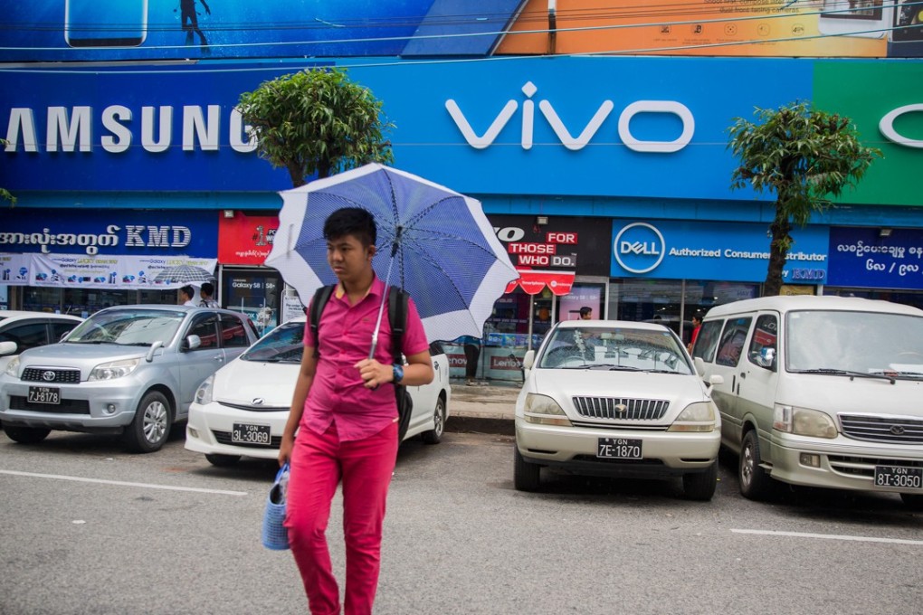 A pedestrian holding an umbrella walks past stores and logos for Samsung Eletronics Co., left, Vivo Communication Technology Co., center, and Oppo Electronics Corp. in Yangon, Myanmar, on Wednesday, June 14, 2017. In 2015, Myanmar signed up more people for mobile phone service than any country in the world except China and India, according to the Asian Development Bank. Photo: Bloomberg