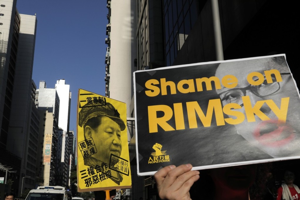Protesters raise a placard to criticise Hong Kong Secretary for Justice Rimsky Yuen as they march in support of young democracy activists. Yuen appealed against the original “lenient” sentencing of the three activists, resulting in them receiving jail time. Photo: AP