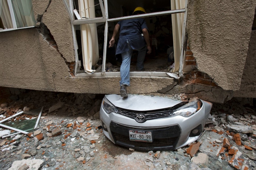 Rodrigo Diaz Mejia climbs over a crushed car into what was a second-story apartment felled by an earthquake last month in the Portales Norte neighbourhood of Mexico City. Photo: AP